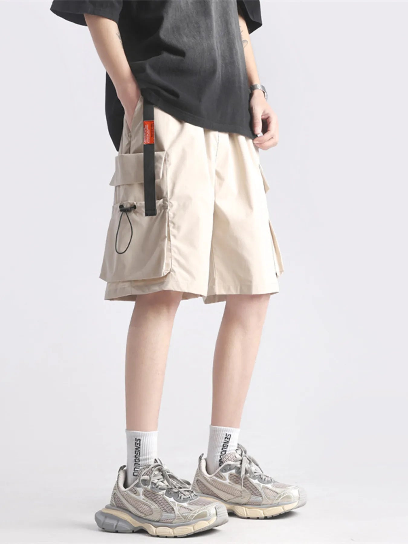 Person wearing beige shorts with multiple pockets on a plain background