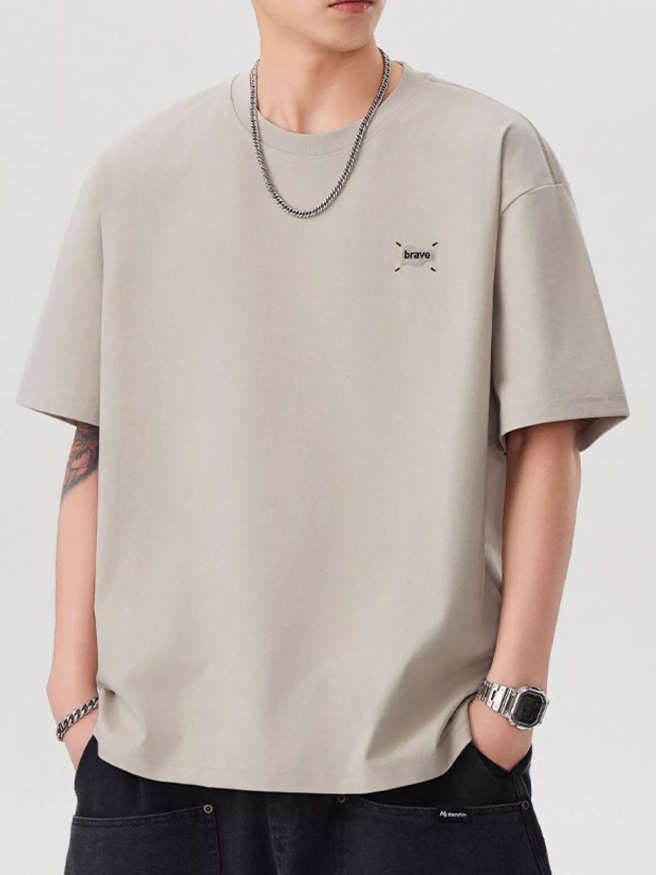 Person wearing a beige t-shirt with a small logo on a plain background