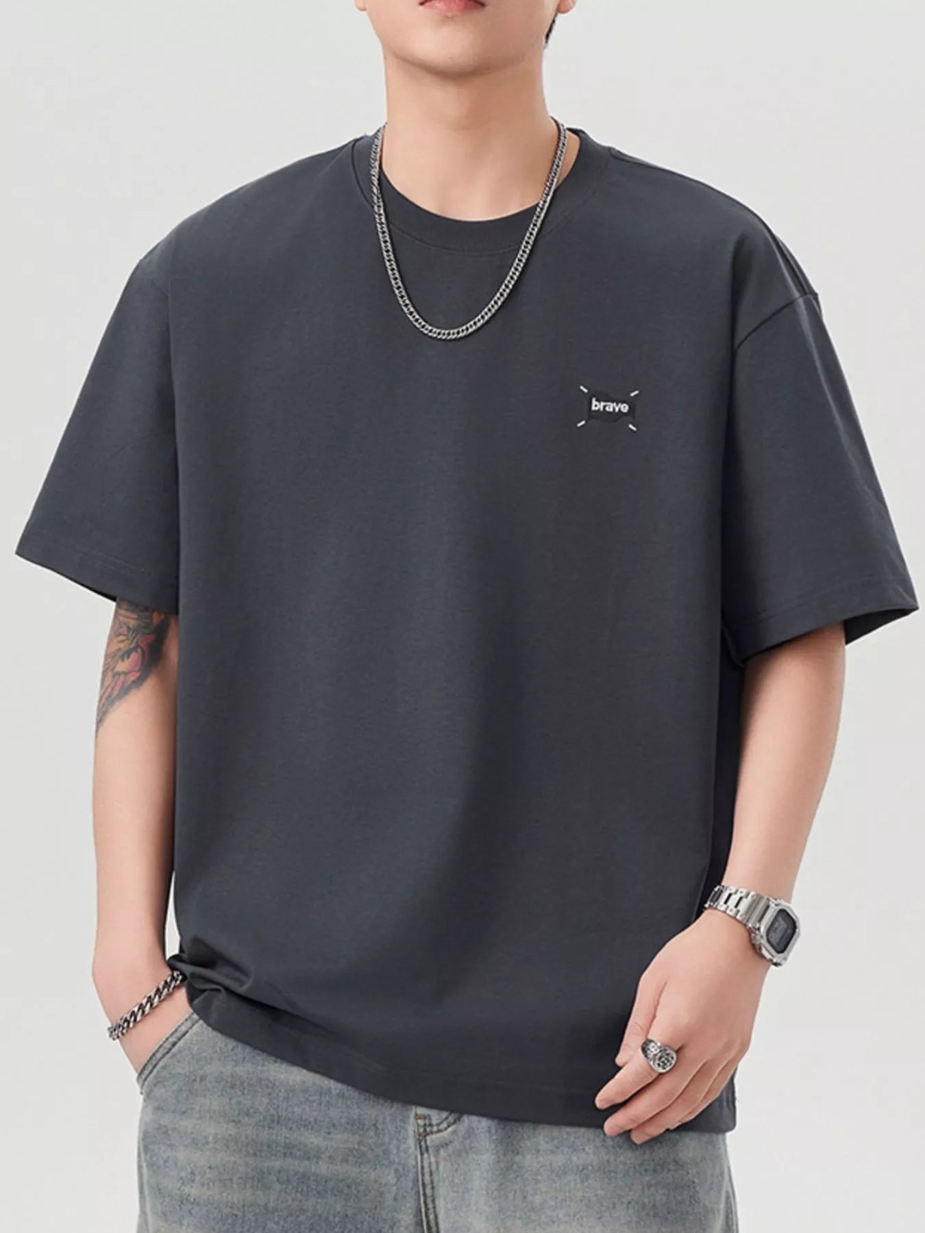 Person wearing a grey t-shirt with a small logo on a plain background