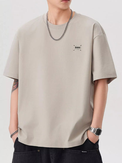 Person wearing a beige t-shirt with a small logo on a plain background