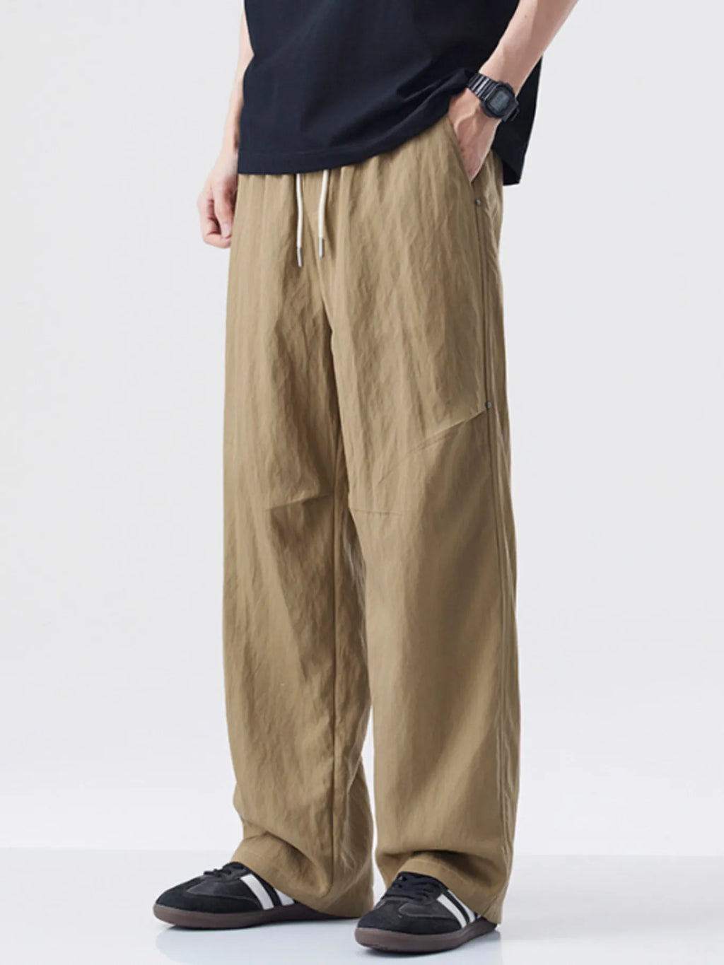 Person wearing beige wide-leg pants and black shoes on a white background