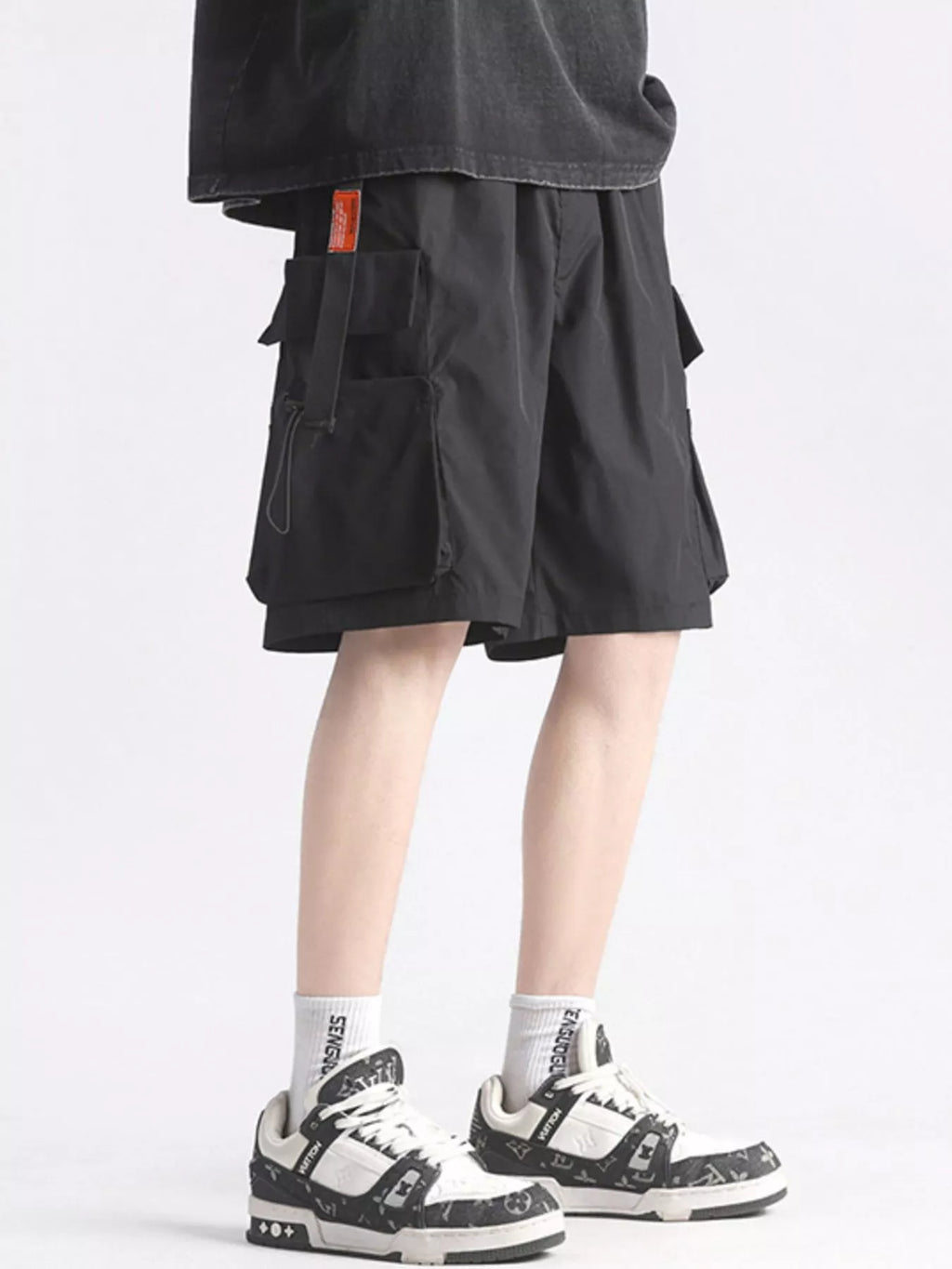Person wearing black cargo shorts and white sneakers on a light gray background