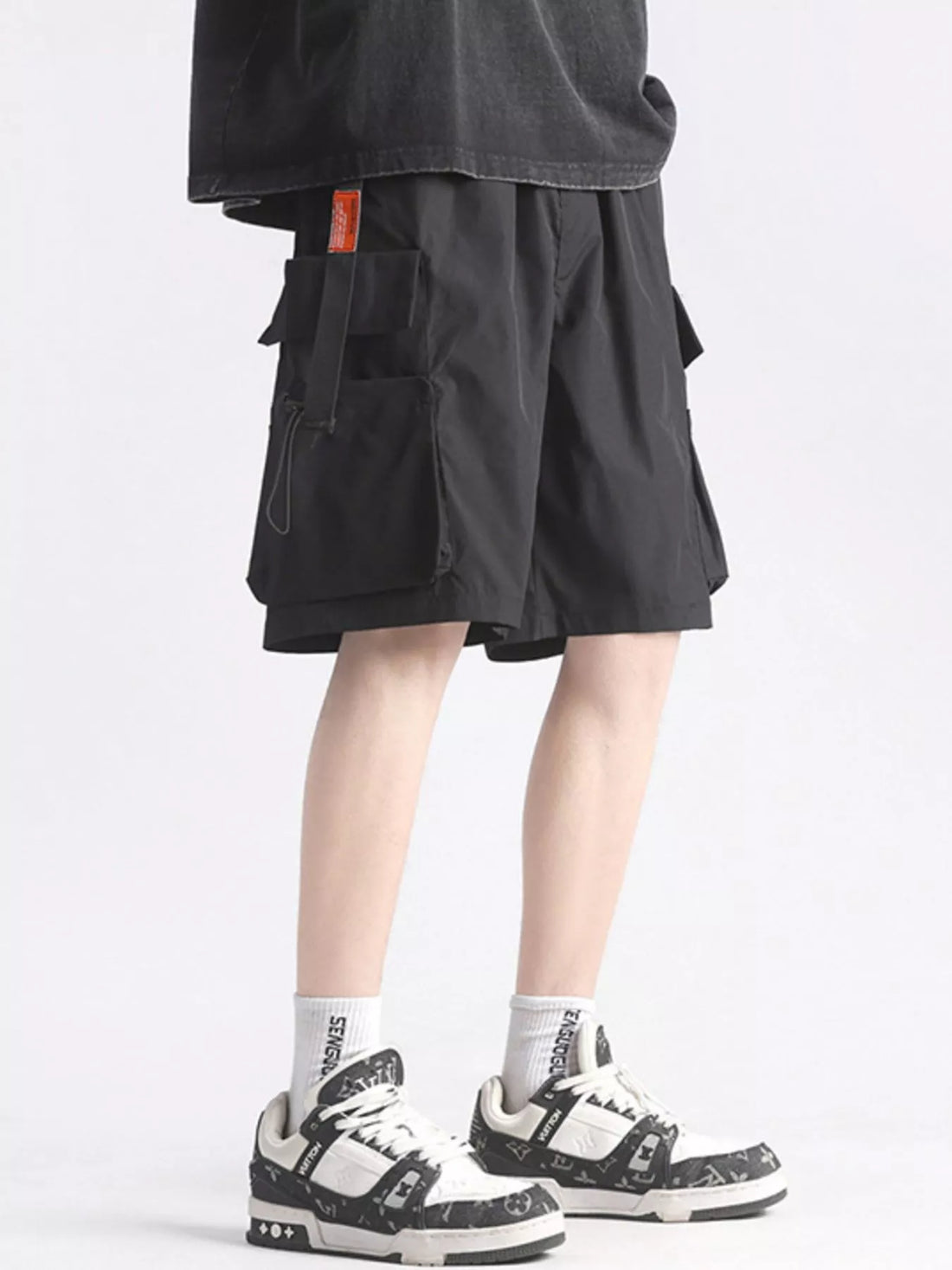 Person wearing black cargo shorts and white sneakers on a light gray background