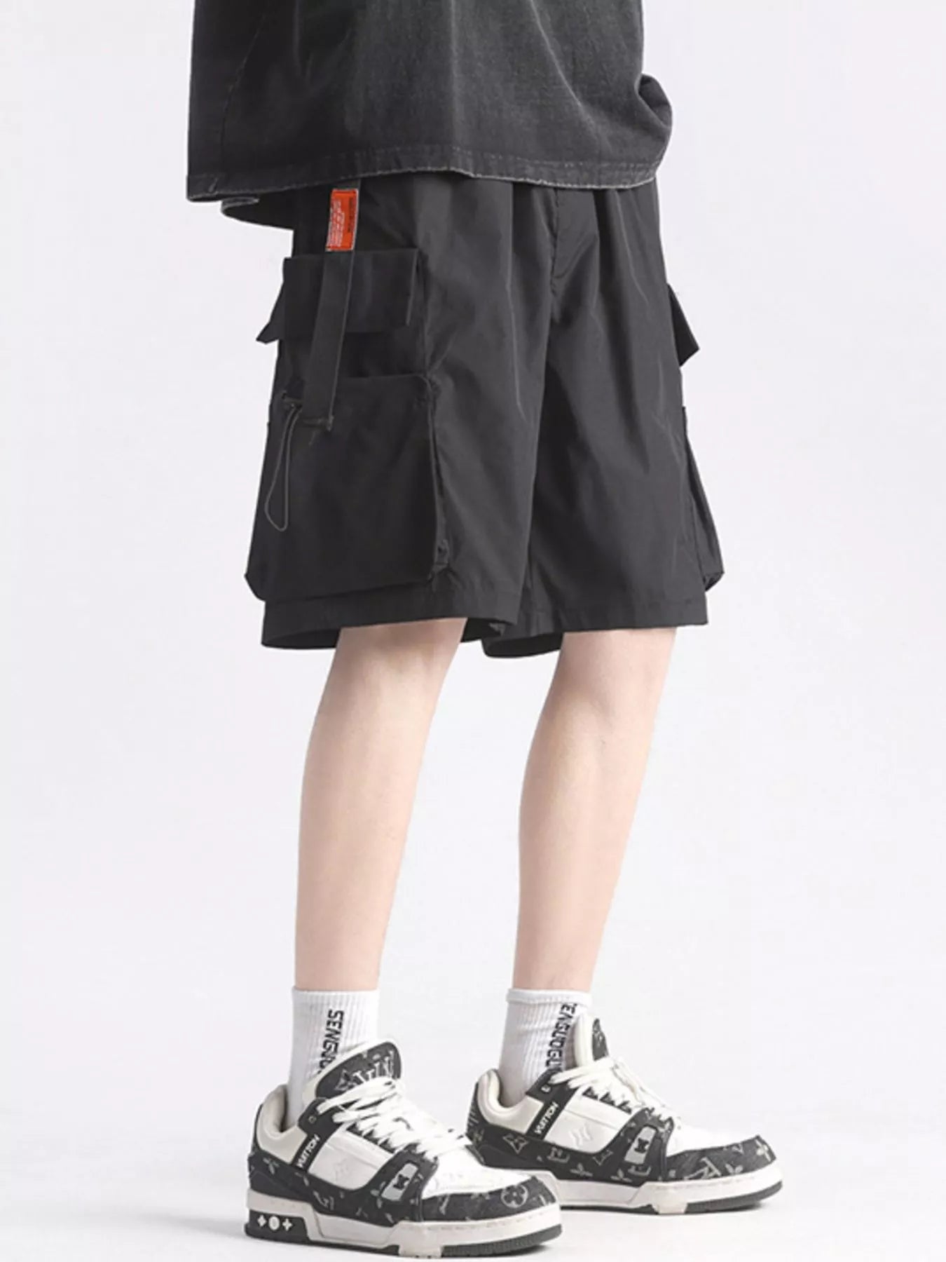 Person wearing black cargo shorts and white sneakers on a light gray background