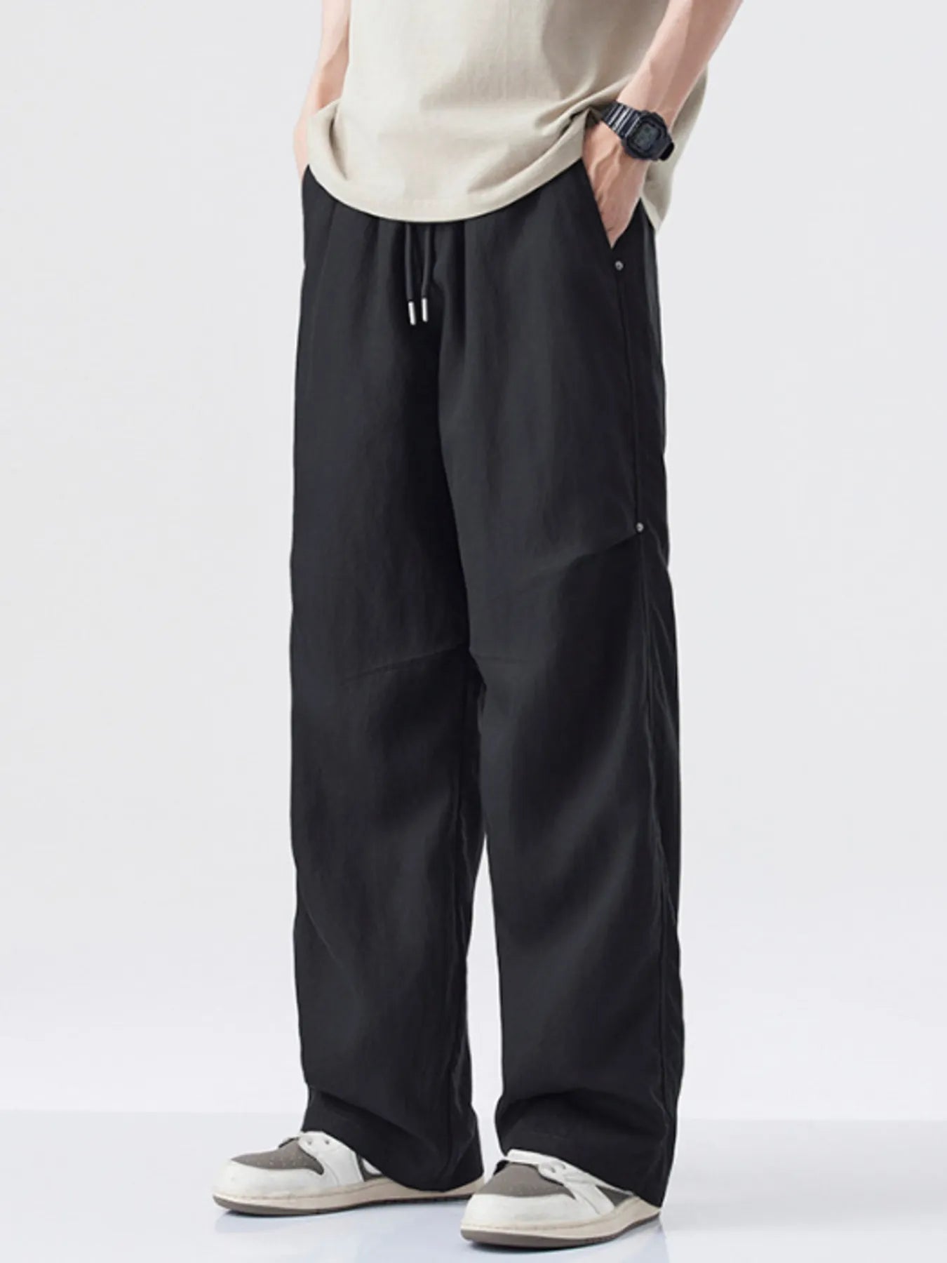 Person wearing black wide-leg pants and a beige top on a white background