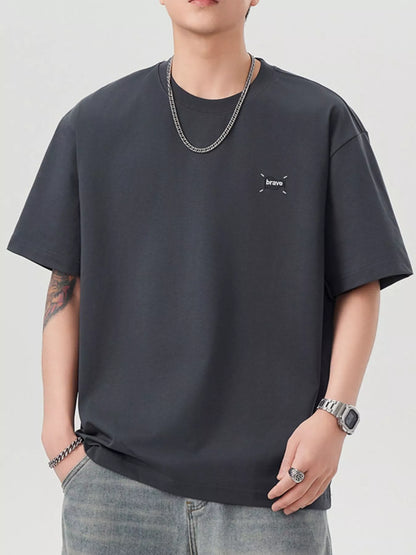 Person wearing a grey t-shirt with a small logo on a plain background