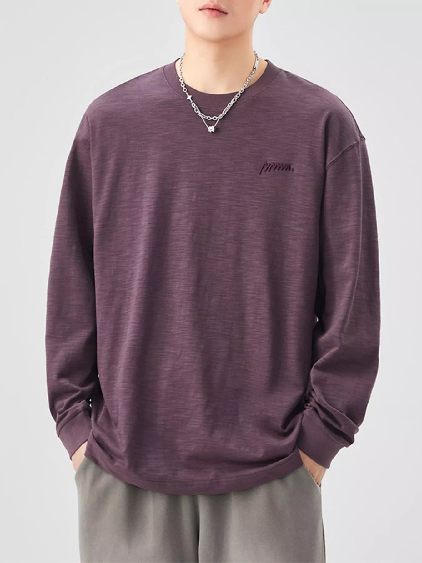 Person wearing a purple long-sleeve shirt with a logo on a plain background