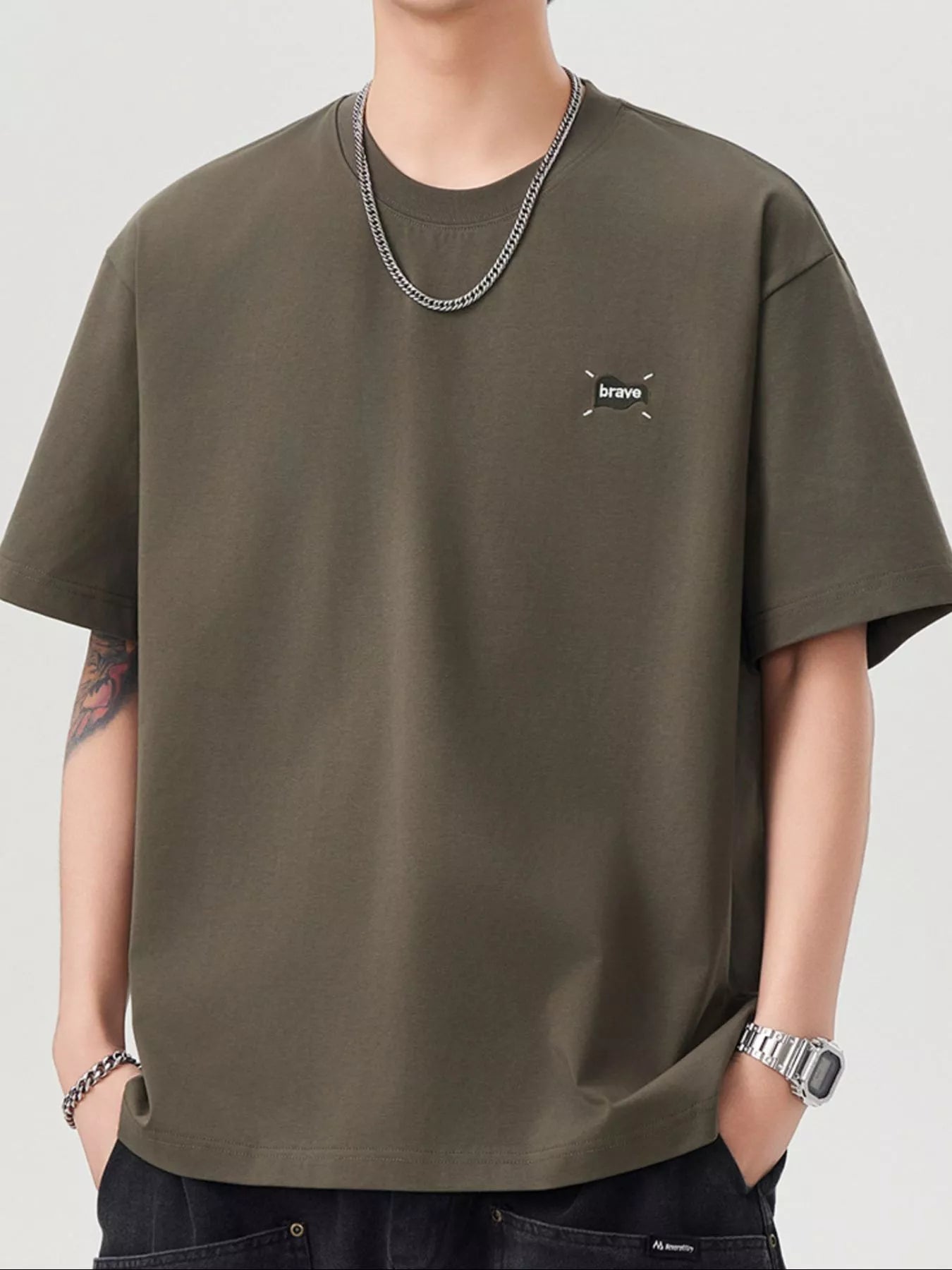 Person wearing an olive green t-shirt with a small logo on a plain background